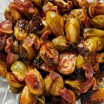 Roasted Brussels sprouts with crispy bacon and a glossy caramelized glaze served on a clear glass plate.