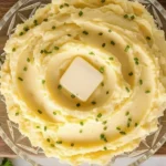 Creamy Yukon Gold Mashed Potatoes topped with butter and chives in a glass bowl on a wooden board