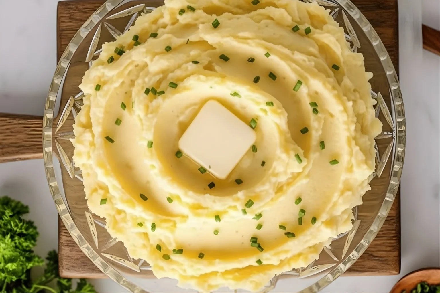 Creamy Yukon Gold Mashed Potatoes topped with butter and chives in a glass bowl on a wooden board