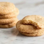 Brown butter shortbread cookies stacked on a marble surface with one cookie showing a bite.