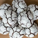 Chewy chocolate crinkle cookies coated in powdered sugar with classic crackled tops on a wooden surface