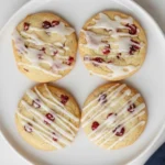 Orange cranberry cookies with icing drizzled on top arranged on a white plate