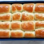 Soft golden Parker House Rolls baked in a blue casserole dish.