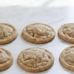 Soft and chewy ginger molasses cookies cooling on a marble countertop