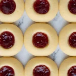 raspberry shortbread thumbprint cookies with smooth buttery dough and bright red jam centers arranged neatly on a marble surface