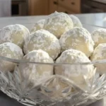 Christmas snowball cookies coated in powdered sugar displayed in a clear glass bowl on a kitchen counter