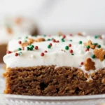 Soft and chewy gingerbread cookie bars topped with creamy frosting and festive red and green sprinkles on a glass plate.