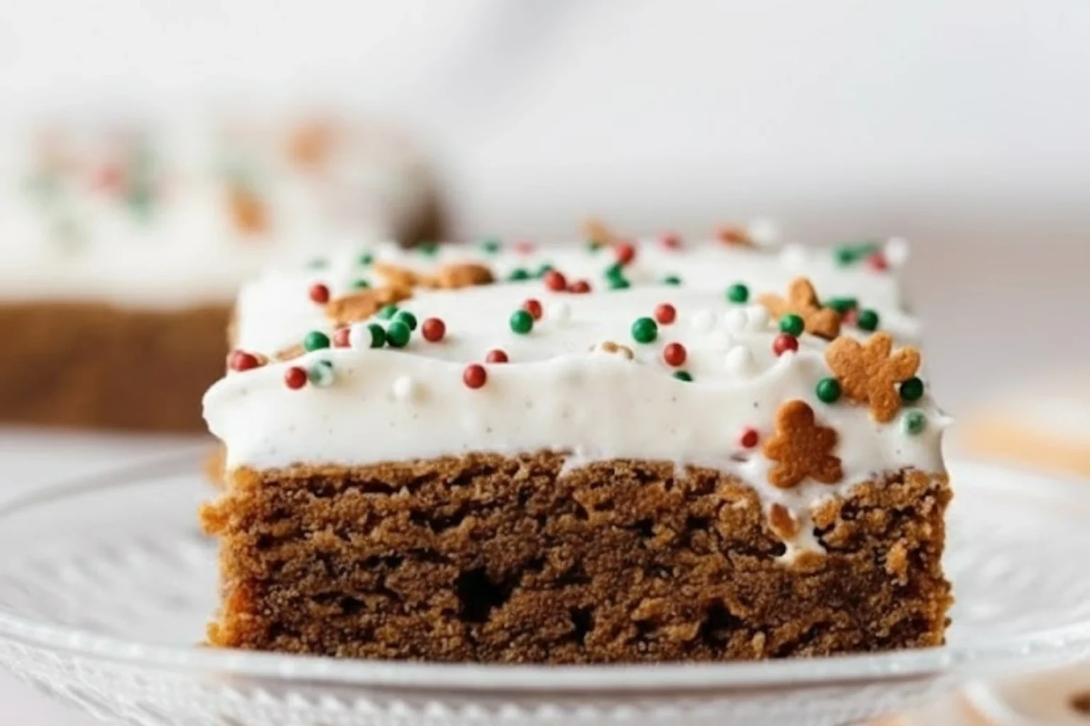 Soft and chewy gingerbread cookie bars topped with creamy frosting and festive red and green sprinkles on a glass plate.