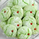 Easy Grinch Cookies on a glass plate dusted with powdered sugar and topped with small red heart sprinkles, perfect for Christmas baking.