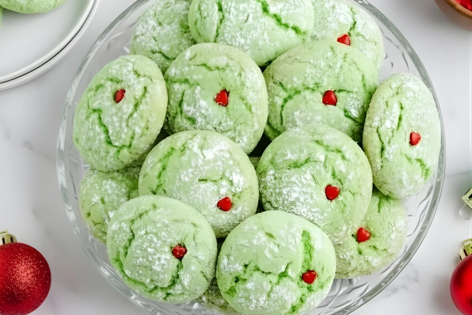Easy Grinch Cookies on a glass plate dusted with powdered sugar and topped with small red heart sprinkles, perfect for Christmas baking.