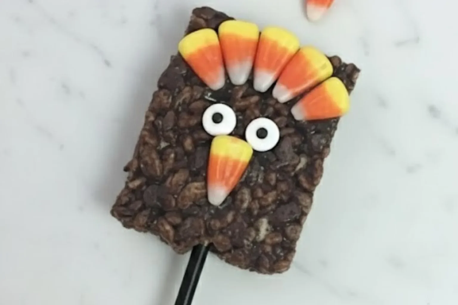 thanksgiving rice krispies treat turkey pop made with chocolate cereal, candy corn feathers, and googly eyes on a stick