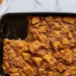 Freshly baked pumpkin bread pudding in a black pan with one slice served on a white plate on a marble counter