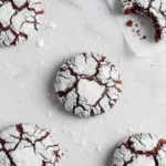 Red velvet crinkle cookies coated in powdered sugar on a marble surface, soft and fudgy with crackled tops and rich cocoa flavor