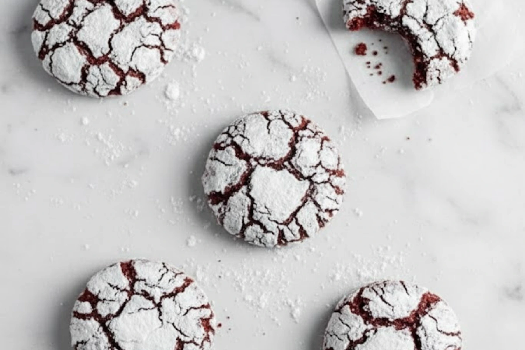 Red velvet crinkle cookies coated in powdered sugar on a marble surface, soft and fudgy with crackled tops and rich cocoa flavor