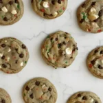 Soft Christmas chocolate chip cookies with white chocolate chips and red and green sprinkles arranged on a white marble surface.