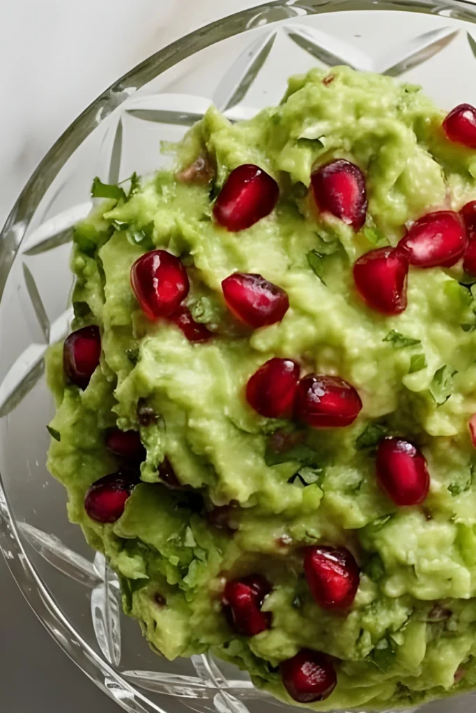 Fresh pomegranate guacamole in a glass bowl with bright red pomegranate seeds and creamy mashed avocado, perfect for a festive appetizer.