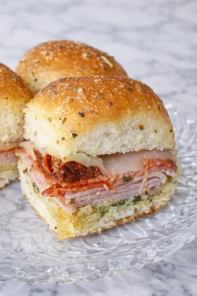 Italian pesto sandwich slider layered with ham salami pepperoni provolone cheese and pesto on a soft golden baked roll
