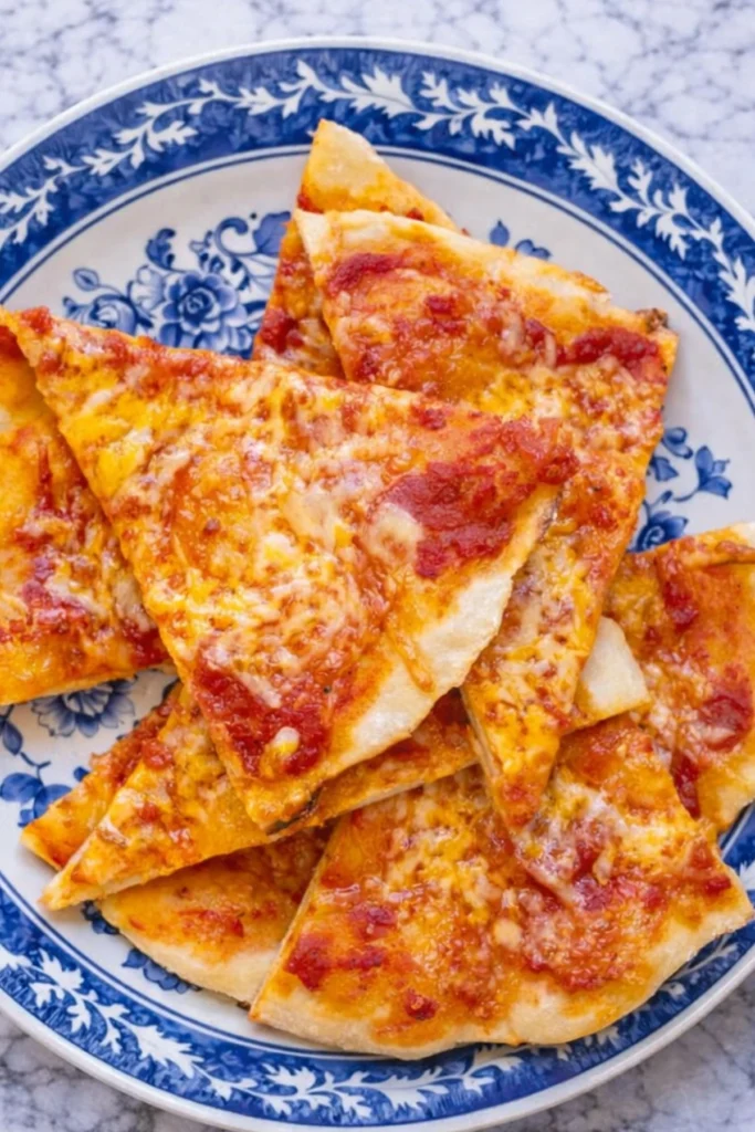 Slices of homemade pizza made with Greek yogurt pizza dough topped with melted cheese and tomato sauce on a blue patterned plate