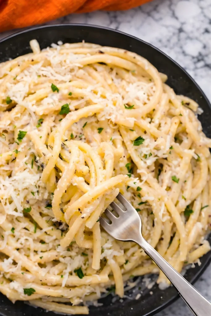 Bucatini Cacio e Pepe twirled on a fork with creamy cheese sauce and fresh parsley