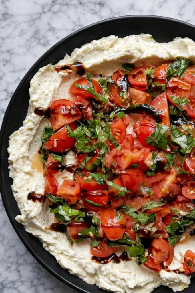Whipped feta bruschetta dip with cherry tomatoes fresh basil and balsamic glaze on black plate