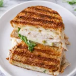 Turkey apple brie panini stacked and cut in half with melted brie sliced turkey crisp apples and arugula on golden grilled bread