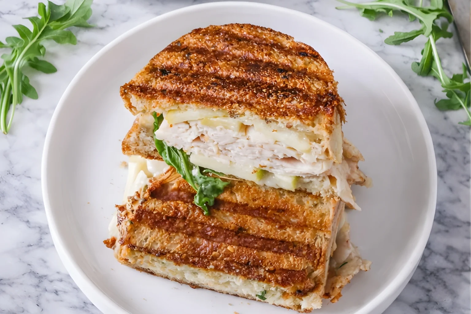 Turkey apple brie panini stacked and cut in half with melted brie sliced turkey crisp apples and arugula on golden grilled bread