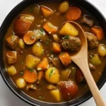 Old Fashioned Beef Stew with tender beef, carrots, potatoes, and celery served in a black bowl.