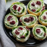 Christmas Cranberry Pinwheels Recipe on black plate with creamy cheese, dried cranberries, and fresh spinach perfect for holiday appetizers