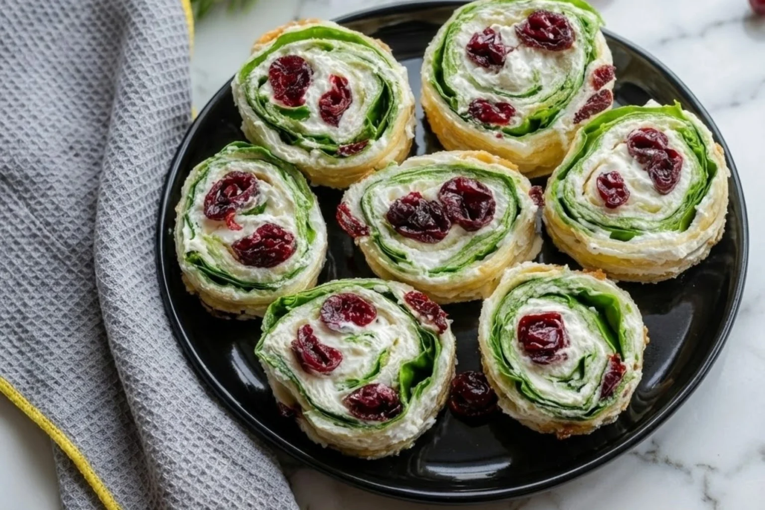Christmas Cranberry Pinwheels Recipe on black plate with creamy cheese, dried cranberries, and fresh spinach perfect for holiday appetizers