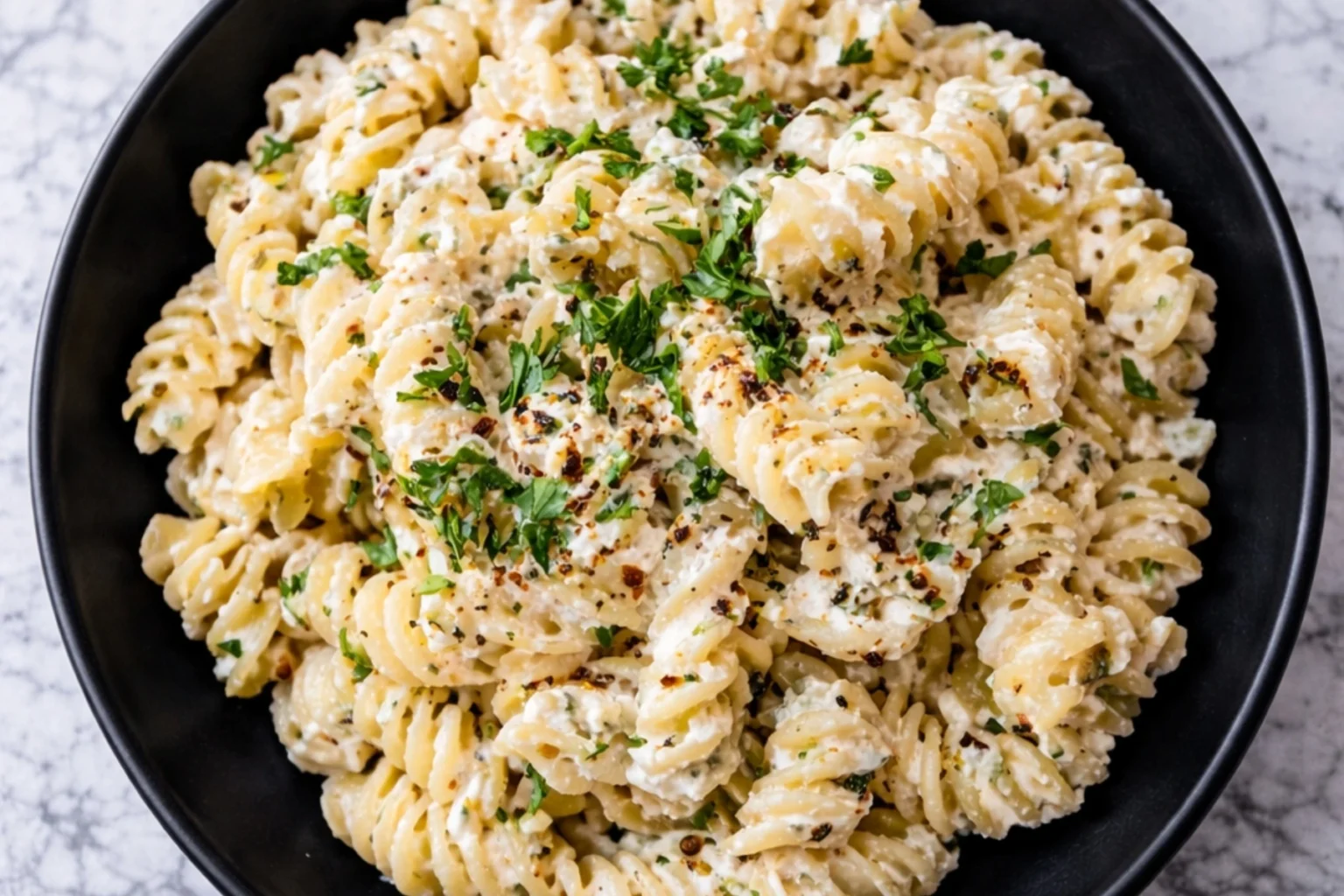 Creamy cottage cheese pasta made with rotini, garlic parmesan sauce, fresh herbs, and cracked black pepper served in a black bowl