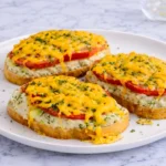 Three open-faced tuna melt sandwiches topped with tomato slices and melted cheddar on toasted bread, garnished with parsley