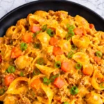 Taco macaroni and cheese with seasoned ground beef, pasta shells, melted cheddar cheese, and green onions in a black bowl