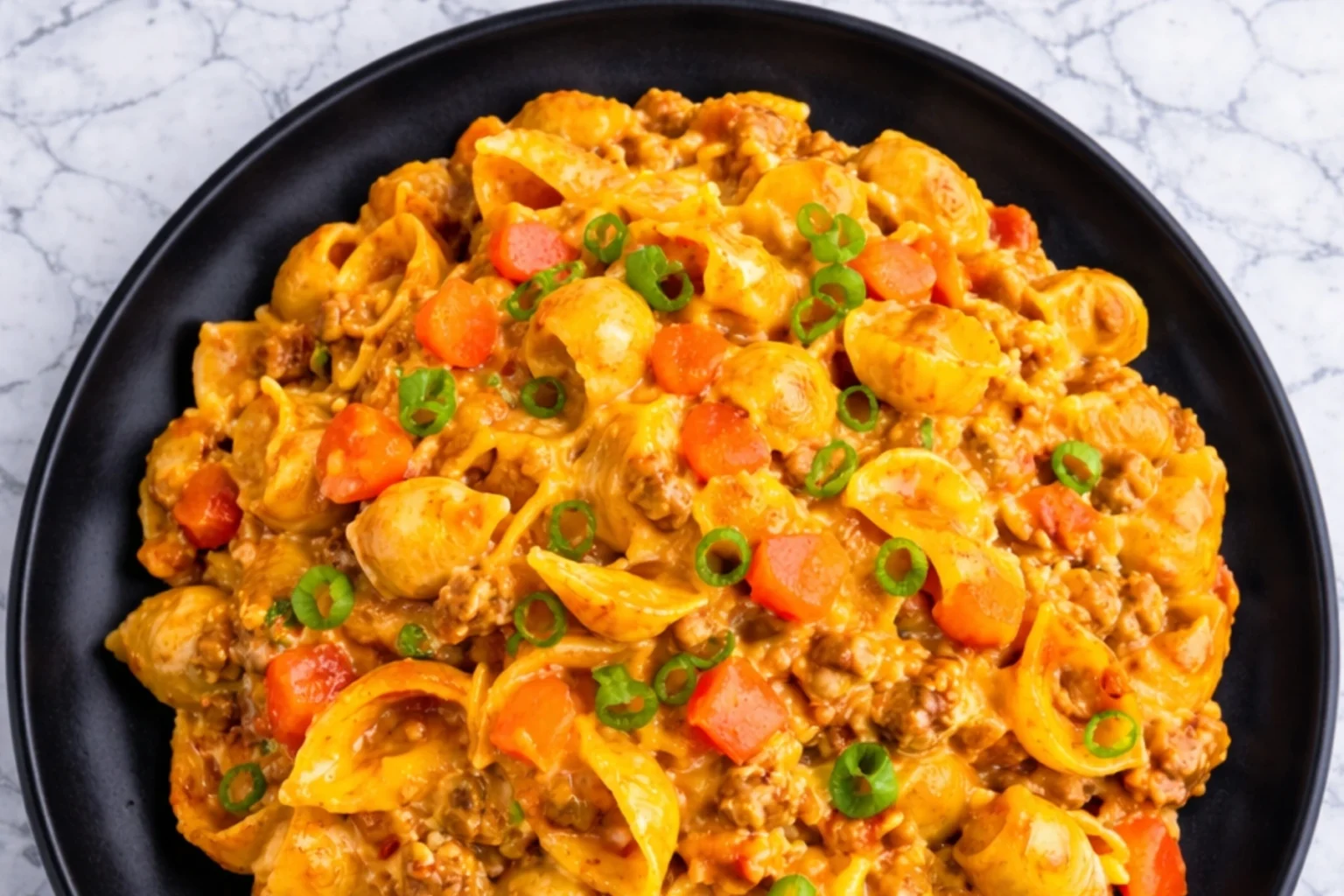 Taco macaroni and cheese with seasoned ground beef, pasta shells, melted cheddar cheese, and green onions in a black bowl