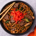 Beef yaki udon noodles with tender steak, vegetables, and savory sauce in a black bowl