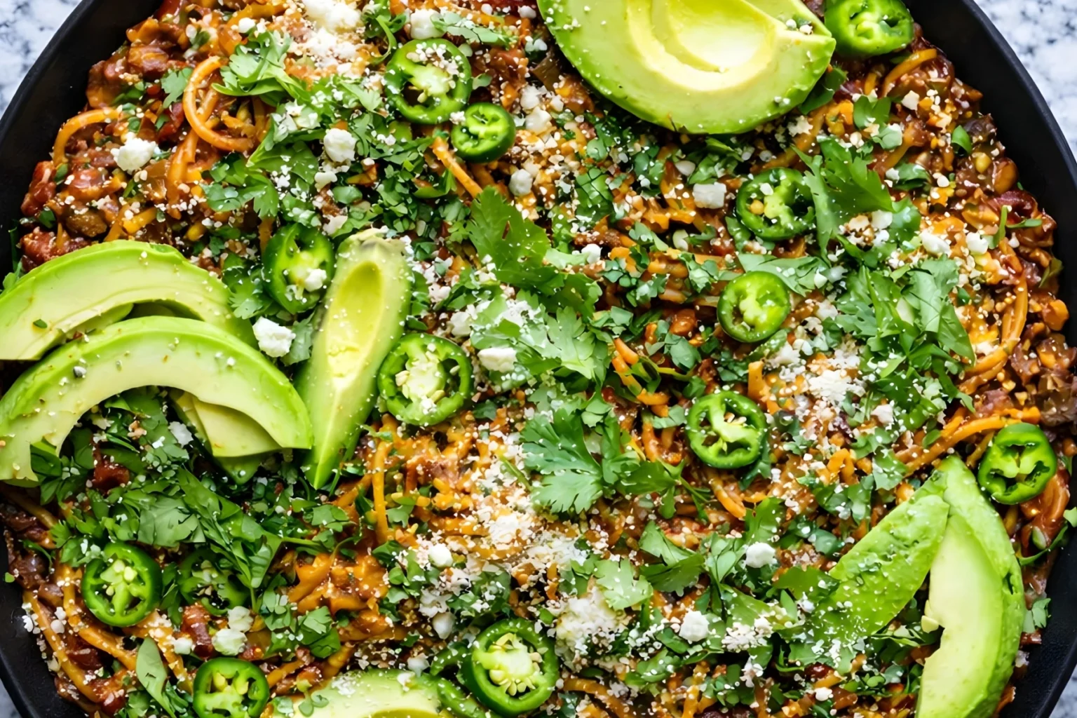 Mexican spaghetti with ground beef, jalapenos, avocado, cilantro, and cotija cheese in a skillet