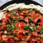 Whipped feta bruschetta dip topped with cherry tomatoes basil and balsamic glaze on a black plate