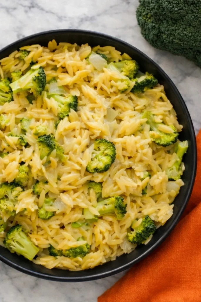 Top-down view of creamy broccoli and orzo skillet with cheddar cheese in a black bowl