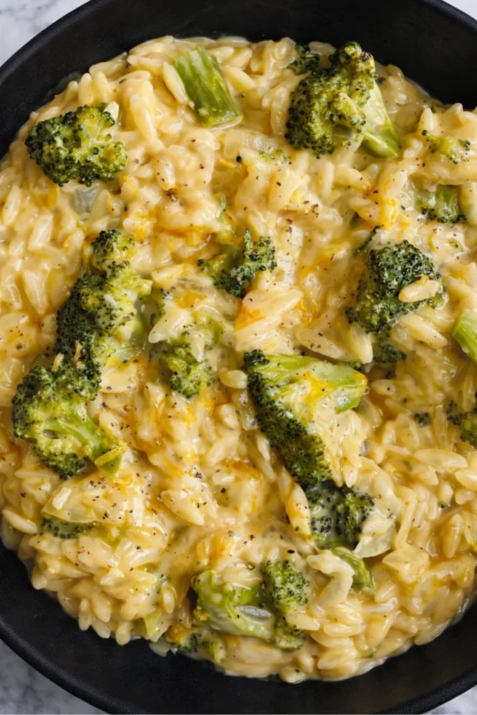Close-up of creamy broccoli cheddar orzo with melted cheese and tender broccoli in a black bowl