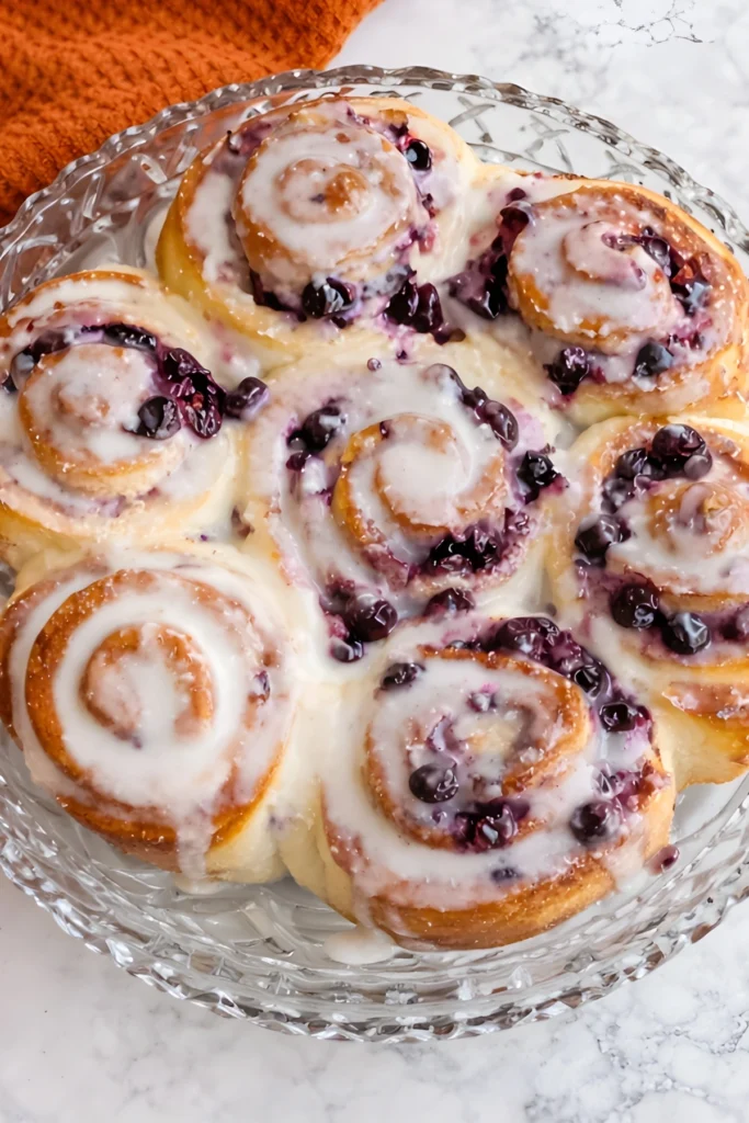 Blueberry lemon sourdough sweet rolls swirled with blueberries and covered in a glossy lemon glaze in a glass baking dish