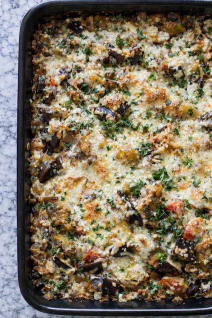 Cheesy baked eggplant casserole with herbs in a black baking dish on marble surface