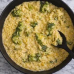 Creamy broccoli cheddar orzo in a black pot with a serving spoon on a marble countertop