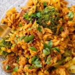 Close-up of vegan sausage and broccoli orzo skillet with chickpeas, fresh herbs, and red pepper flakes served on a glass plate with a gold fork