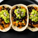 Quinoa and black bean tacos topped with guacamole, red onion, and cilantro on flour tortillas