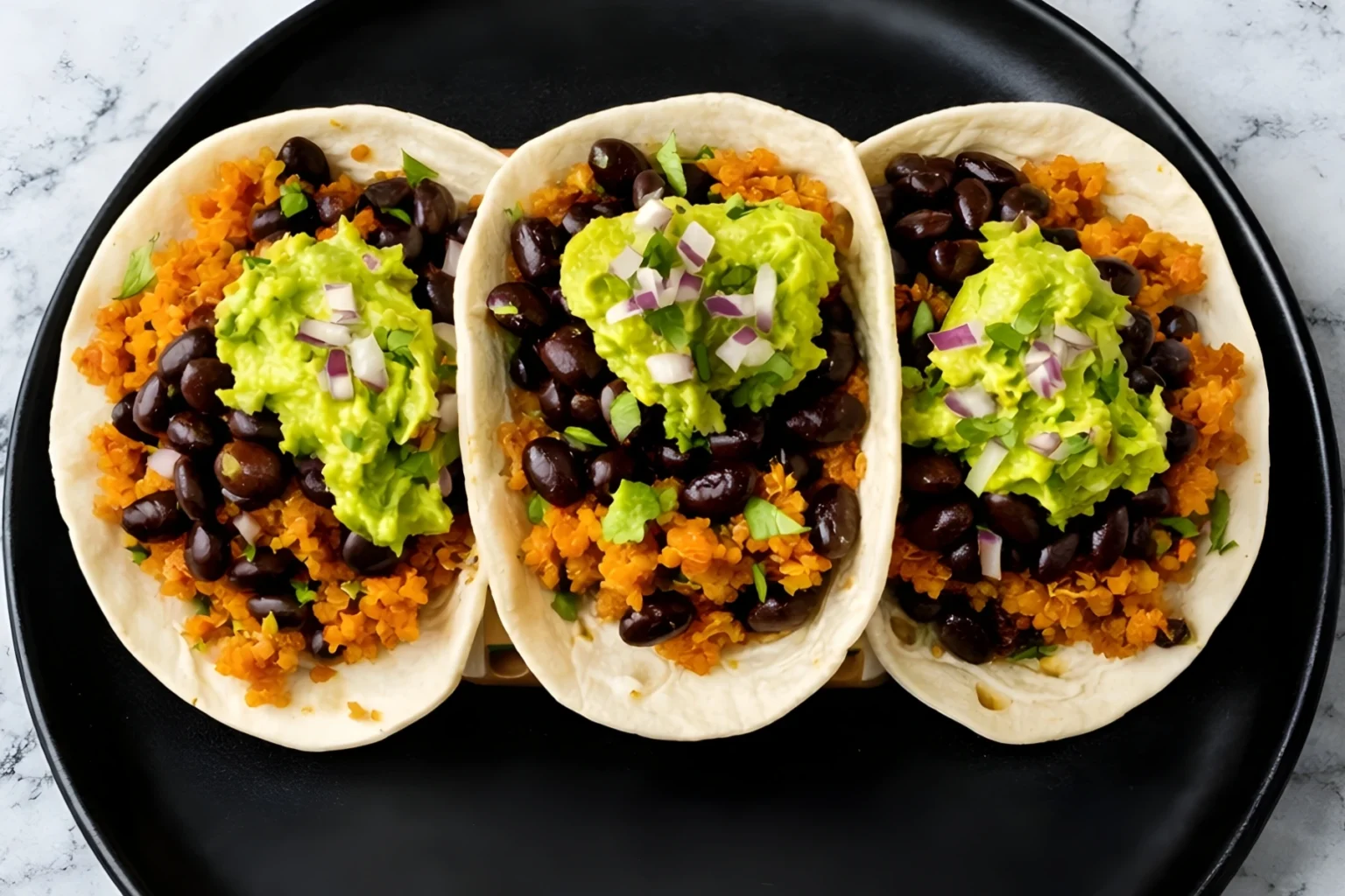 Quinoa and black bean tacos topped with guacamole, red onion, and cilantro on flour tortillas