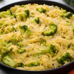 Creamy broccoli and orzo skillet with melted cheddar cheese in a black bowl