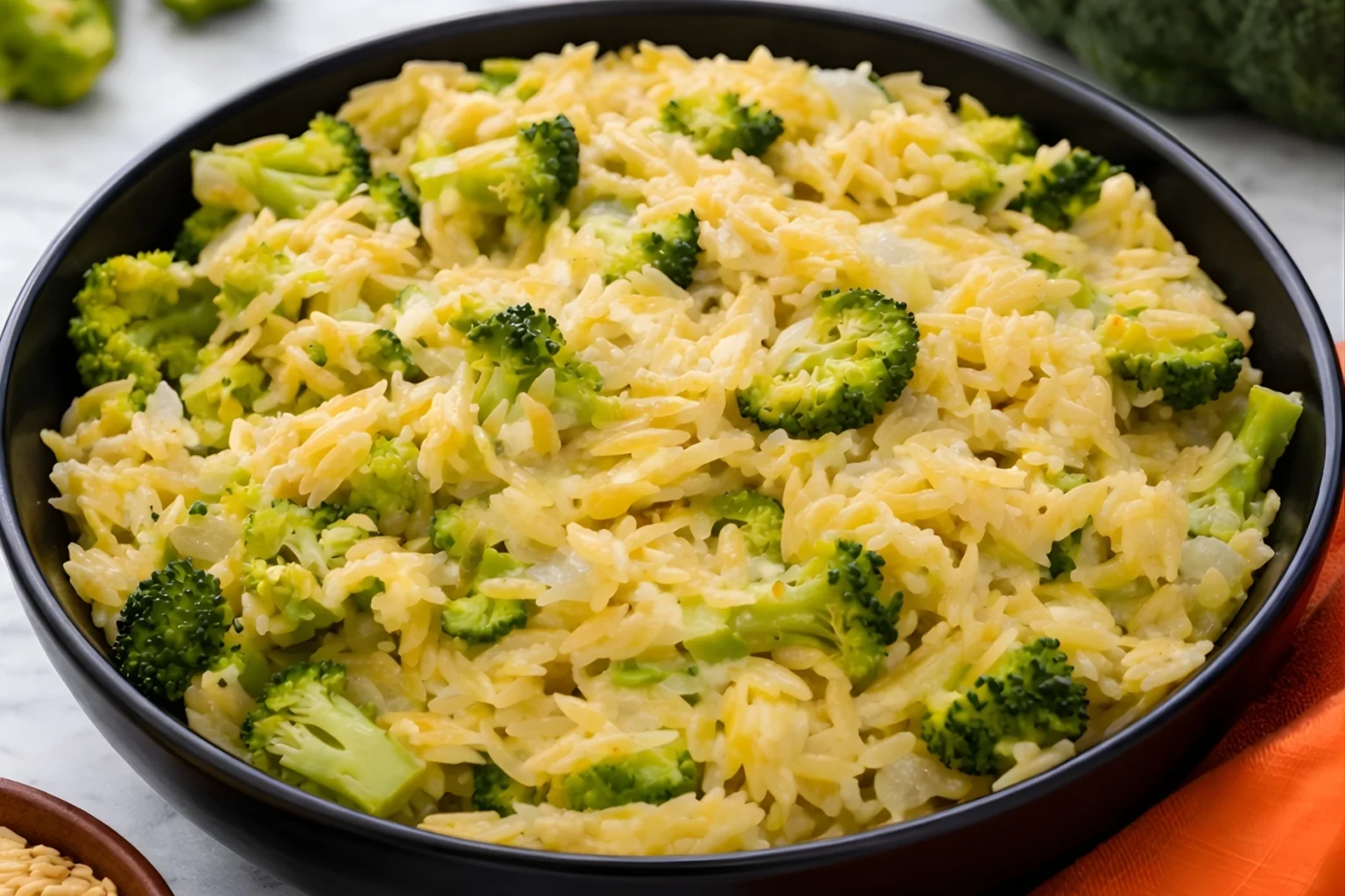 Creamy broccoli and orzo skillet with melted cheddar cheese in a black bowl