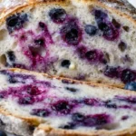 Homemade lemon blueberry sourdough bread sliced open revealing purple berry streaks and open crumb structure with lemons