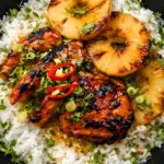 Grilled Hawaiian chicken with caramelized pineapple rings over coconut rice, garnished with fresh herbs and sliced red chili
