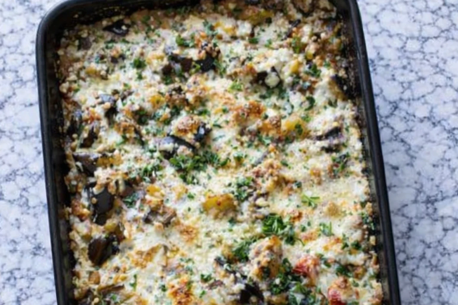 Baked eggplant casserole with melted cheese herbs and vegetables in a casserole dish