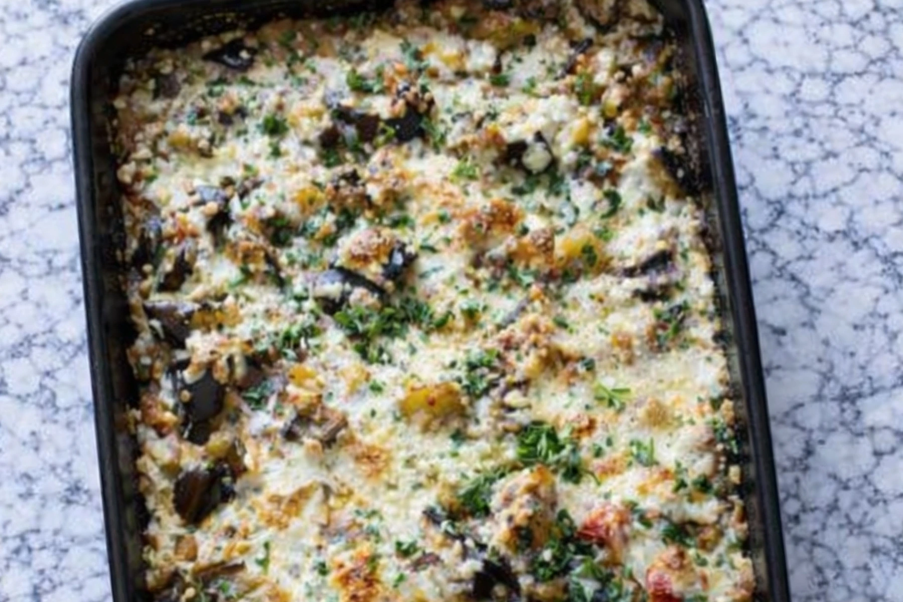 Baked eggplant casserole with melted cheese herbs and vegetables in a casserole dish